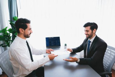 Resmi ofiste takım elbise giyen kendine güvenen bir adam, iş görüşmesi sırasında özgeçmiş kağıtlarını tutuyor. Sorular soran, aday yeterliliği ve iş için uygunluk değerlendirmesi yapan bir muhabir. Coşkulu