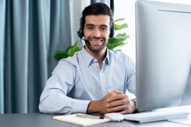 Erkek çağrı merkezi operatörü ya da telesales temsilcisi masasında oturmuş kulaklık takıyor. İş yerinde kameraya gülümseyen müşteri temsilcisi. coşkulu