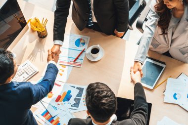 Grup iş adamları toplantı masasında el sıkışırken üst açıdan kendilerine güvenirler. Genç işadamı ve işkadını işçiler yatırım anlaşması imzaladılar. Jivy