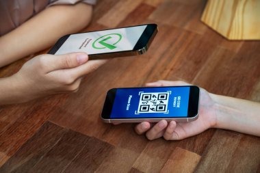 QR kodu parasız ödeme taraması için ekranda gösterilir. Kapalı eller, mobil uygulamadan elektronik işlem yoluyla para aktarmak için akıllı telefonu tutuyor. Hızlı ödeme için barkod teknolojisi. Coşkulu.
