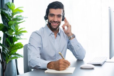 Erkek çağrı merkezi operatörü ya da telesales temsilcisi masasında oturmuş kulaklık takıyor. İş yerinde kameraya gülümseyen müşteri temsilcisi. coşkulu