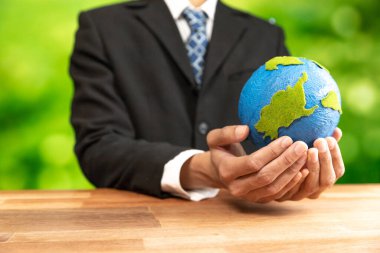 İşadamı temiz enerji ve sıfır CO2 emisyonu kullanarak sürdürülebilir dünya için çevresel farkındalığın sembolü olarak kağıt toprağı elinde tutuyor. Dünya 'yı kurtarmak için yeşil politikası olan çevre dostu bir şirket. Değiştir