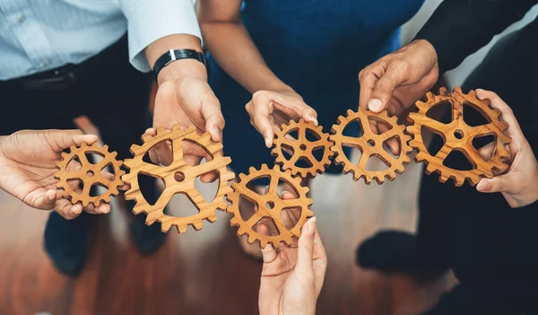 Office worker holding cog wheel as unity and teamwork in corporate workplace concept. Diverse colleague business people showing symbol of visionary system and mechanism for business success. Concord