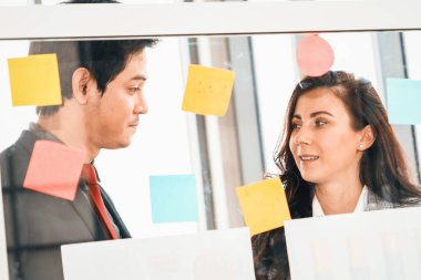İş adamları ofisteki proje planlama kurulunda çalışıyor ve proje gelişimini analiz etmek için iş arkadaşlarıyla sohbet ediyorlar. Düzenli olması için cama yapıştırılmış yapışkan notlar kullanıyorlar. Jivy