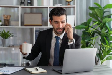 Çalışkan işadamı, ofisindeki dizüstü bilgisayarla cep telefonlu, modern, çalışkan ofis çalışanı yaşam biçimi konsepti olarak çalışırken müşterileriyle telefonda konuşmakla meşgul. Coşkulu