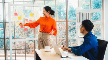 İş adamları ofisteki proje planlama kurulunda çalışıyor ve proje gelişimini analiz etmek için iş arkadaşlarıyla sohbet ediyorlar. Düzenli olması için cama yapıştırılmış yapışkan notlar kullanıyorlar. Jivy