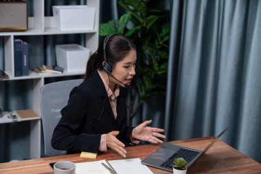 Bilgisayarında mikrofon ve kulaklıkla Asyalı çağrı merkezi çalışıyor. Kadın operatör istisnai müşteri hizmetleri sunar. Destek veren çağrı merkezi ajanı, müşteriye soruşturmada yardım ediyor. Coşkulu.