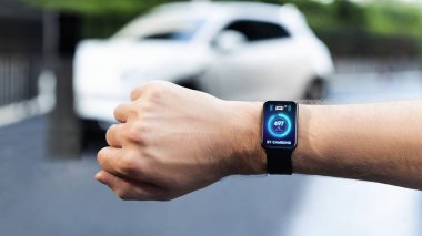 İş adamı, istasyonun otoparkından şarj olurken akıllı ekranda EV akü durumunu kontrol ediyor. EV teknolojisi adaptasyonu için temiz enerjinin gelecekteki yaşam tarzı. İnceleyin