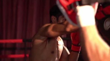 Asyalı ve Kafkasyalı Muay Thai boksörü boks antrenmanında boks antrenmanında boks antrenörüne yumruk atma, Muay Thai boks tekniği ve becerilerini sergileme. Impetus