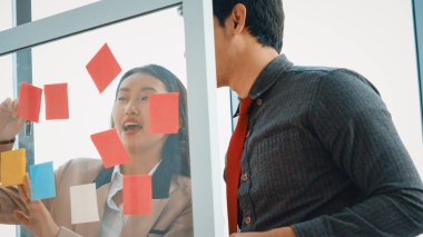 İş adamları ofisteki proje planlama kurulunda çalışıyor ve proje gelişimini analiz etmek için iş arkadaşlarıyla sohbet ediyorlar. Düzenli olması için cama yapıştırılmış yapışkan notlar kullanıyorlar. Jivy