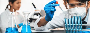 Kendini adamış bir grup bilim adamı tıbbi laboratuvarda kimyasal deney yapıyor. Aşı ilacı veya antibiyotik geliştirmek için pipetten deney tüpüne kesin miktarda sıvı döküyorlar. Neoterik