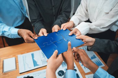 Şirket çalışanı, yapboz parçalarını masa üzerindeki raporlara ortaklık ve takım çalışması olarak bağlıyor. Yapboz 'u birleştirerek iş dünyasındaki birlik ve sinerji. Uyum