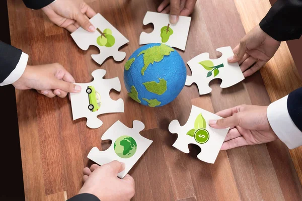 Cohesive group of business people holding eco icon jigsaw puzzle pieces around globe Earth as eco corporate responsibility for community and sustainable solution for greener Earth. Quaint