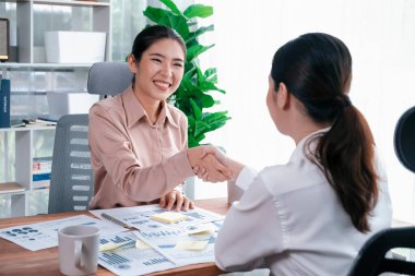 İki Asyalı iş kadını, iş yeri konseptinde takım çalışması ve dürüstlüğün önemi olarak, gösterge paneli veri kağıtlarının yığınlarını başarıyla analiz ettikten sonra modern ofiste el sıkışıyor. Coşkulu.