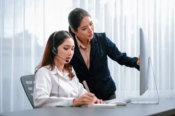 Asian female customer support operator wearing headset is guided by her supportive manager. Experienced colleague help operator handle a call with a client, providing advice and guidance. Enthusiastic