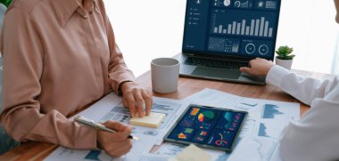 Analist ekip arkadaşı dijital gösterge panelinde finansal verileri tartışır, grafikleri dizüstü bilgisayar ve tablet ekranda analiz eder. Modern ofis pazarlama planlamak için iş zekasını kullanır. Coşkulu.