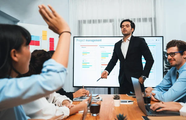 Corporate employee raise hand ask question during project meeting, businessman or manager explaining business task planning schedule with timeline software show on TV screen. Habiliment