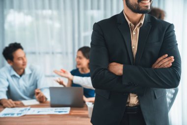 İş adamı, toplantı odasının arka planında çeşitli iş arkadaşlarıyla güven içinde poz veriyor. Çok kültürlü ekip iş başarısı için birlikte çalışır. Modern iş adamı portresi. Uyum