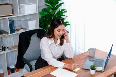 Genç hevesli iş kadını iş görüşmesinde konuşuyor ve laptopuna çoklu ofis hanımı olarak notlar yazıyor. Müşterilerle telefonda konuşurken iş ödevleri yazan kadın çalışan.
