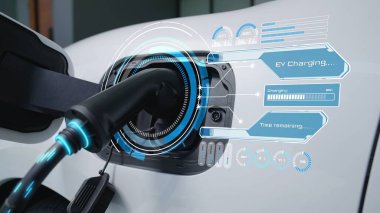 Ev şarj istasyonundaki EV şarj cihazı fişe takılı ve dijital batarya durum hologramını gösteren elektrikli arabayı şarj ediyor. Akıllı ve fütüristik ev enerjisi altyapısı. İnceleyin