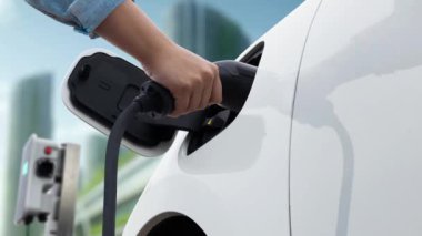 Adam elektrikli arabaya akıllı EV şarj cihazı takıyor ve arka planda modern şehir manzarası olan EV şarj istasyonundan şarj oluyor. ESG şehrinde gelecekteki sürdürülebilir güç ve EV araba kullanımı. İnceleyin