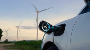 Elektrikli araba, EV şarj istasyonundan enerji alıyor. Rüzgar türbini çiftliğinde EV şarj kablosu kablosunun fütüristik akıllı batarya durum hologramını gösteriyor. Alternatif temiz enerji sürdürülebilirliği. İnceleyin