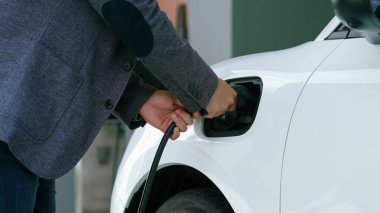 İlerici adam evindeki elektrikli aracın aküsüne emisyonsuz güç bağlantısı kuruyor. Elektrikli araç elektrik istasyonundan EV araba aküsüne kabloyla şarj oluyor.