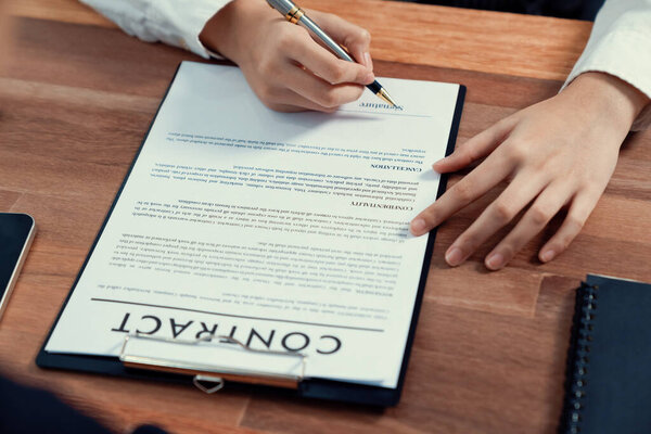 Closeup hand signing contract document with pen, sealing business deal with signature. Businesspeople finalizing business agreement by writing down signature on contract paper. Enthusiastic