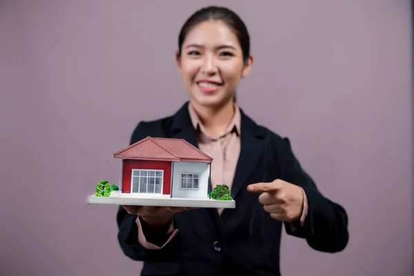 年轻的亚洲女人穿着正式的西服 带着和展示独立背景的房子模型 理想的住房广告 家庭保险促销 或可定制的复制空间 很有激情 — 图库照片