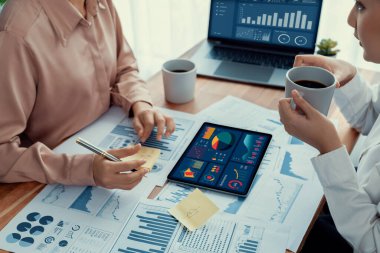 Analist ekip arkadaşı dijital gösterge panelinde finansal verileri tartışır, grafikleri dizüstü bilgisayar ve tablet ekranda analiz eder. Modern ofis pazarlama planlamak için iş zekasını kullanır. Coşkulu.