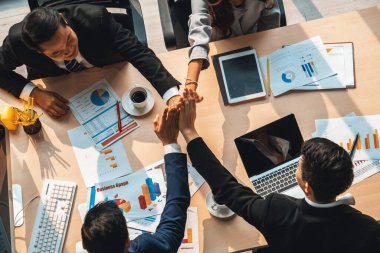 Mutlu iş adamları takım çalışmasının başarısını kutlarken ofis masasında yukarıdan çekilen neşeyle kutluyorlar. Genç işadamı ve işkadını işçiler, neşeli zafer gösterisi birliği desteği gösterdiler. Jivy