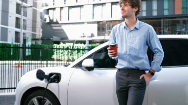 İlerici işadamı, şehir merkezinde dolaşmadan önce şarj cihazından elektrikli arabasına şarj prizi takıyor. Çevre dostu şarj edilebilir araba, sürdürülebilir ve temiz enerjiyle çalışıyor..
