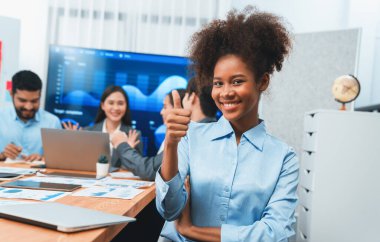 Bir grup ofis çalışanı ile birlikte arka planda ekranda gösterim paneliyle buluşan mutlu Afrikalı genç bir iş kadını portresi. Takım toplantısında kendine güveni tam bir ofis hanımı. Uyum