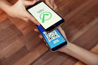 QR kodu parasız ödeme taraması için ekranda gösterilir. Kapalı eller, mobil uygulamadan elektronik işlem yoluyla para aktarmak için akıllı telefonu tutuyor. Hızlı ödeme için barkod teknolojisi. Coşkulu.