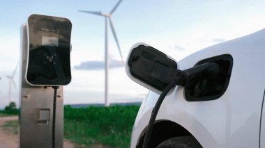 Çevreyi korumak için rüzgar türbininden yeşil ve yenilenebilir enerjiyle çalışan şarj istasyonunda şarj edilen gelişmiş gelecek enerji altyapısı konsepti.