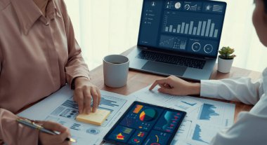 Analist ekip arkadaşı dijital gösterge panelinde finansal verileri tartışır, grafikleri dizüstü bilgisayar ve tablet ekranda analiz eder. Modern ofis pazarlama planlamak için iş zekasını kullanır. Coşkulu.