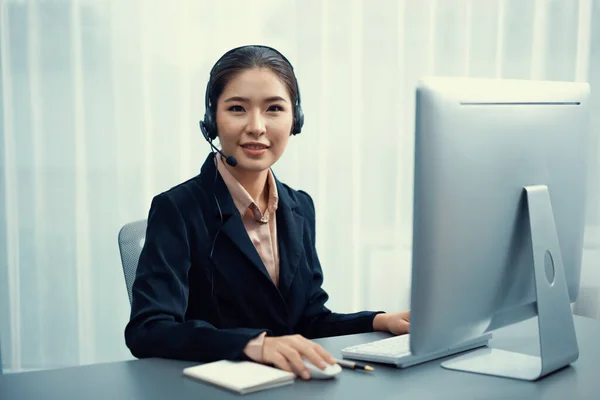 Asian call center with headset and microphone working on her workspace looking at camera. Female operator provide exceptional customer service. Supportive call center agent portrait. Enthusiastic