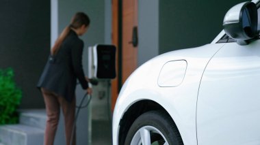 Bir kadın evinde elektrikli araç şarj aletinin fişini çekiyor. İlerici bir yaşam tarzında elektrikli araçların kullanımı, temiz ve sağlıklı bir çevreye katkıda bulunur..
