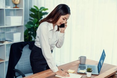 Genç hevesli iş kadını iş görüşmesinde konuşuyor ve laptopuna çoklu ofis hanımı olarak notlar yazıyor. Müşterilerle telefonda konuşurken iş ödevleri yazan kadın çalışan.