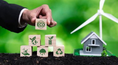 İşadamı, ECO küp sembolünü ev ve rüzgar türbini modeliyle piramit üst rafına koydu. Orman yenilenmesi ve yeşil çevre için alternatif temiz enerji kullanarak doğal farkındalık. Değiştir
