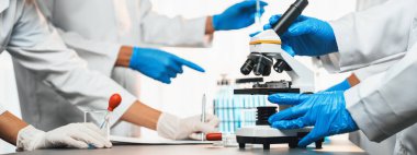 Kendini adamış bir grup bilim adamı yeni bir aşı ilacı ya da antibiyotik geliştirmek için tıbbi laboratuvarda mikroskop kullanarak kimyasal deney yapıyorlar. Biyoteknoloji laboratuvarı ve tıp araştırma konsepti. Neoterik