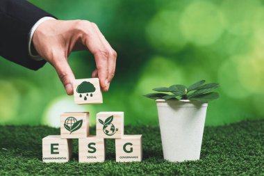 İş adamı elinde ESG küp sembollü saksı tutuyor. Orman yenilenmesi ve doğal farkındalık. Çevre dostu politikayla birlikte, ekolojiyi korumak için yenilenebilir enerji kullanan etik yeşil iş. Değiştir