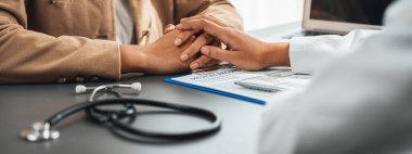 Doktor, doktor kliniğinde destekleyici ve profesyonel olduğu için genç hasta elini tutarken tıbbi teşhis raporunu ve şefkatli bir sağlık hizmeti danışmanlığı sunduğunu göster. Neoterik