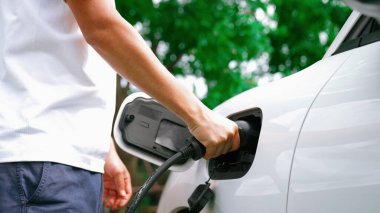 İlerici adam elektrikli aracına elektrik kablosu takıyor. Ev şarj istasyonundan EV arabası. Çevreyi korumak için temiz ve yenilenebilir enerji kullanan elektrikli bir araba. Çevre dostu otomobil.