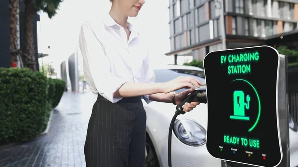 ビジネスマンは 市内中心部や公共駐車場の充電ステーションから彼女の電気自動車を充電します 代替クリーンエネルギーを使用して環境に優しい充電式車 Peruse — ストック写真