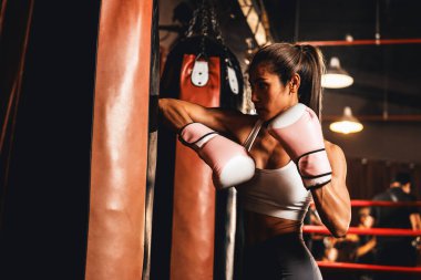 Asyalı kadın Muay Thai boksörü boks antrenmanında dirsek atağı yapıyor, boks malzemelerini tekmelemek için dirsek darbesi yapıyor, Muay Tai boks tekniği ve becerilerini sergiliyor. Impetus