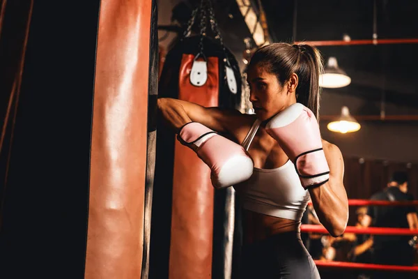 Asian female Muay Thai boxer unleash elbow attack in fierce boxing training session, delivering elbow strike to kicking bag boxing equipment, showcasing Muay Thai boxing technique and skill. Impetus