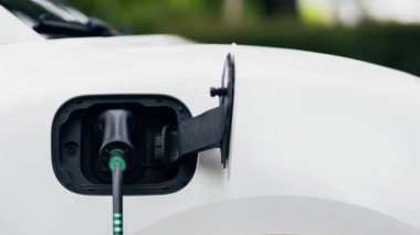 Ön görüş EV şarj cihazı, elektrik yükleme istasyonundan parlayan ışık kablosu ile elektrik yüklemek için elektrikli arabaya takıldı. Kesme-Sınır yeniliği ve gelecekteki yeşil enerji sürdürülebilirliği. İnceleyin