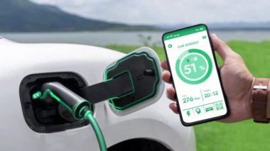 Akıllı telefon ekran akü durumu arayüzünü elinde tutan iş adamı akıllı EV mobil uygulama ile EV otomobili elektrik şarj istasyonundan doğal göl arka planı ile elektrik. İnceleyin.
