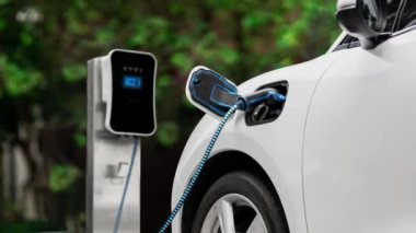 Doğal yeşil araba parkındaki ekolojik temiz enerji şarj istasyonundan gelen fütürist akıllı EV şarj aletinin şarj ettiği elektrikli araba. Alternatif enerji kullanan gelecekçi çevre dostu elektrikli araba. İnceleyin